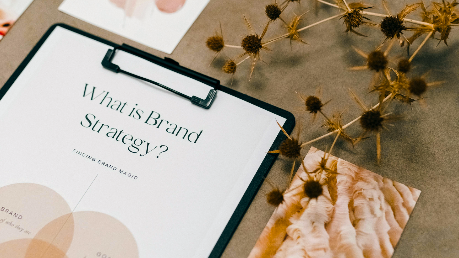 A strategic brand identity document titled 'What is Brand Strategy?' on a clipboard, surrounded by design mood board elements.