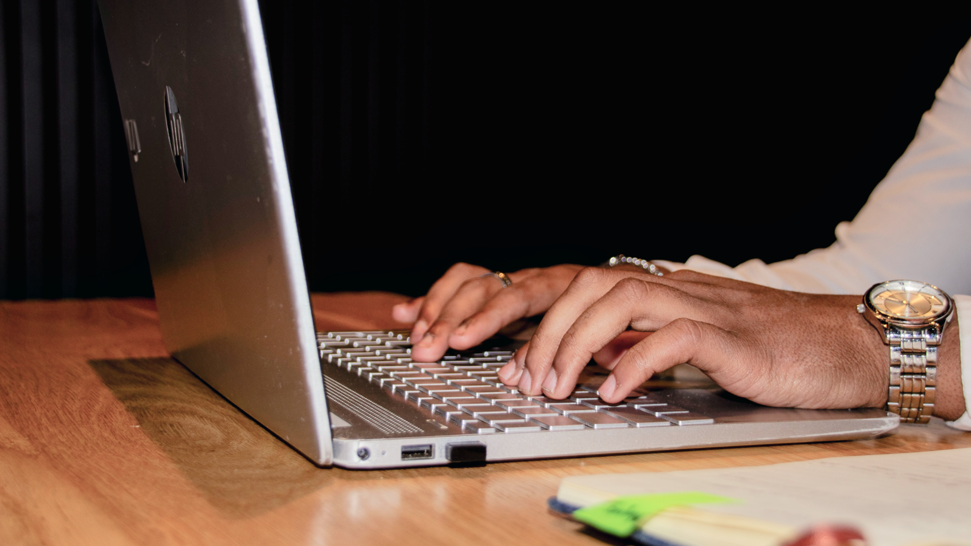 A close-up of a professional's hands typing on a silver HP laptop at a wooden desk, representing data-driven innovation and technical precision.