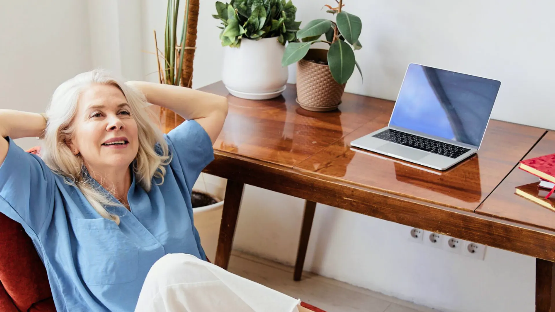 A relaxed business owner leaning back with hands behind her head in a bright home office with a laptop and plants, representing the peace of mind that comes with clear digital knowledge.